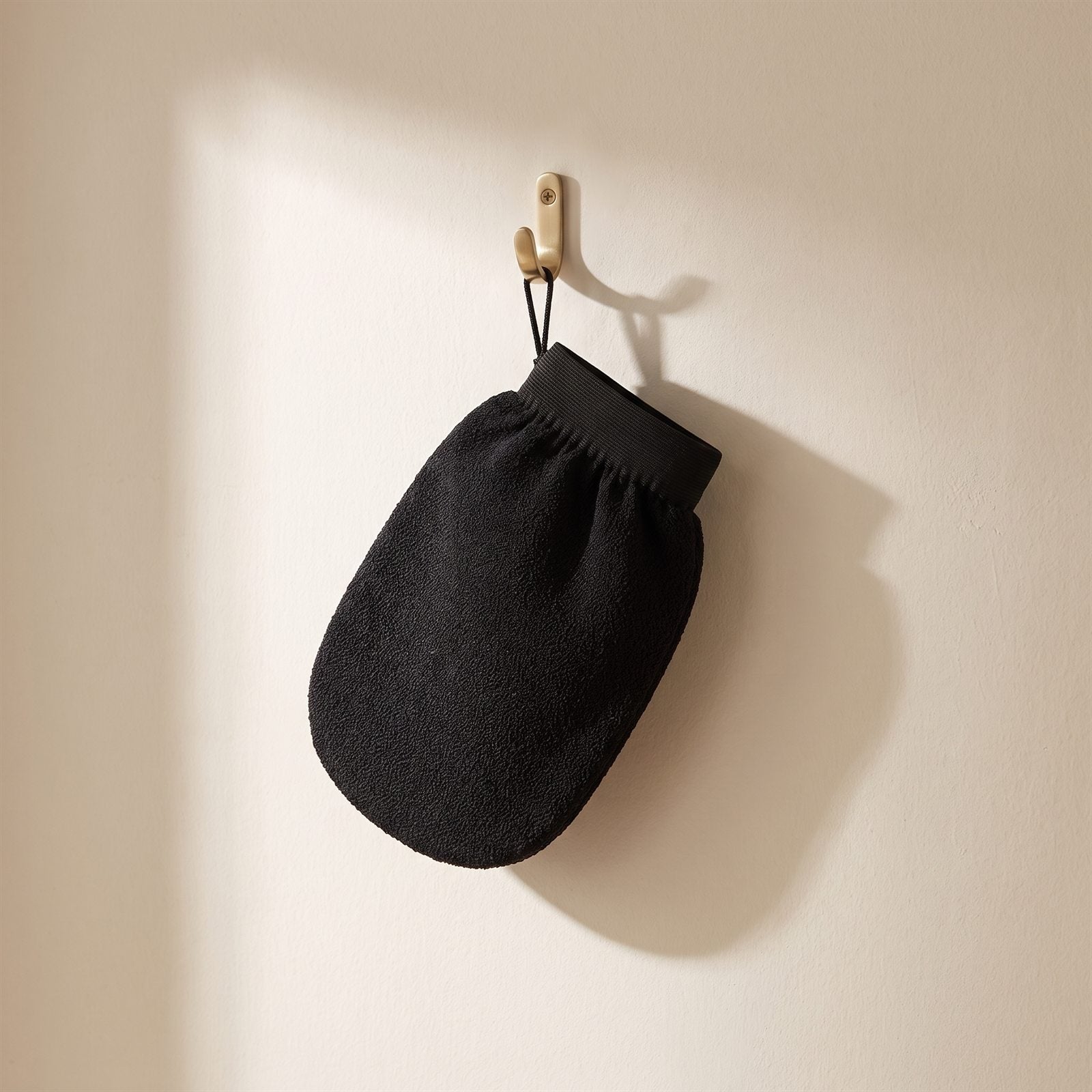 Exfoliating mitt hanging by its loop from a brass hook to dry