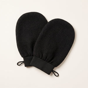 Pair of black Korean exfoliating bath mitts on an off-white background